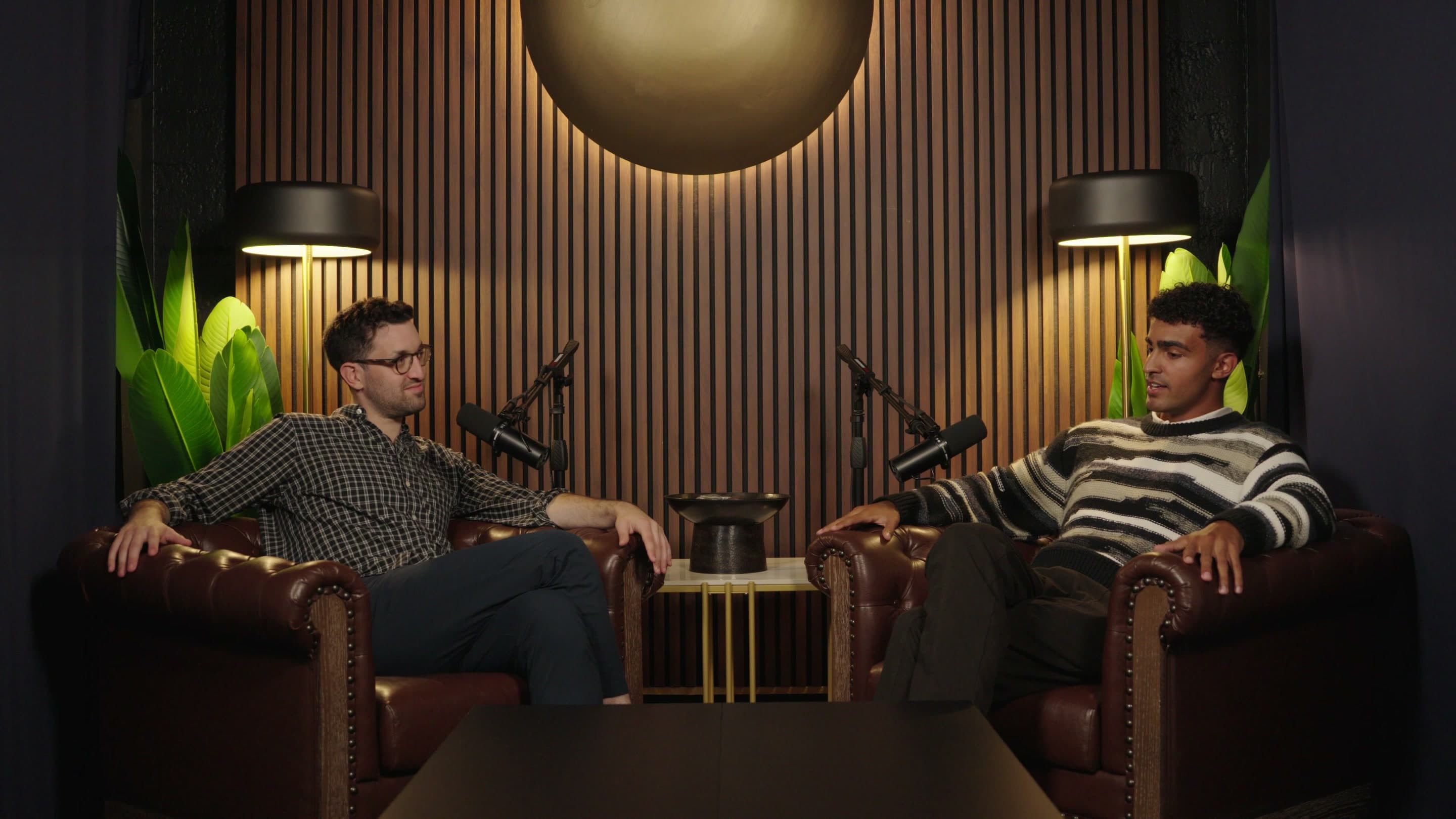 A podcast set with two hosts in leather armchairs and an empty table between them